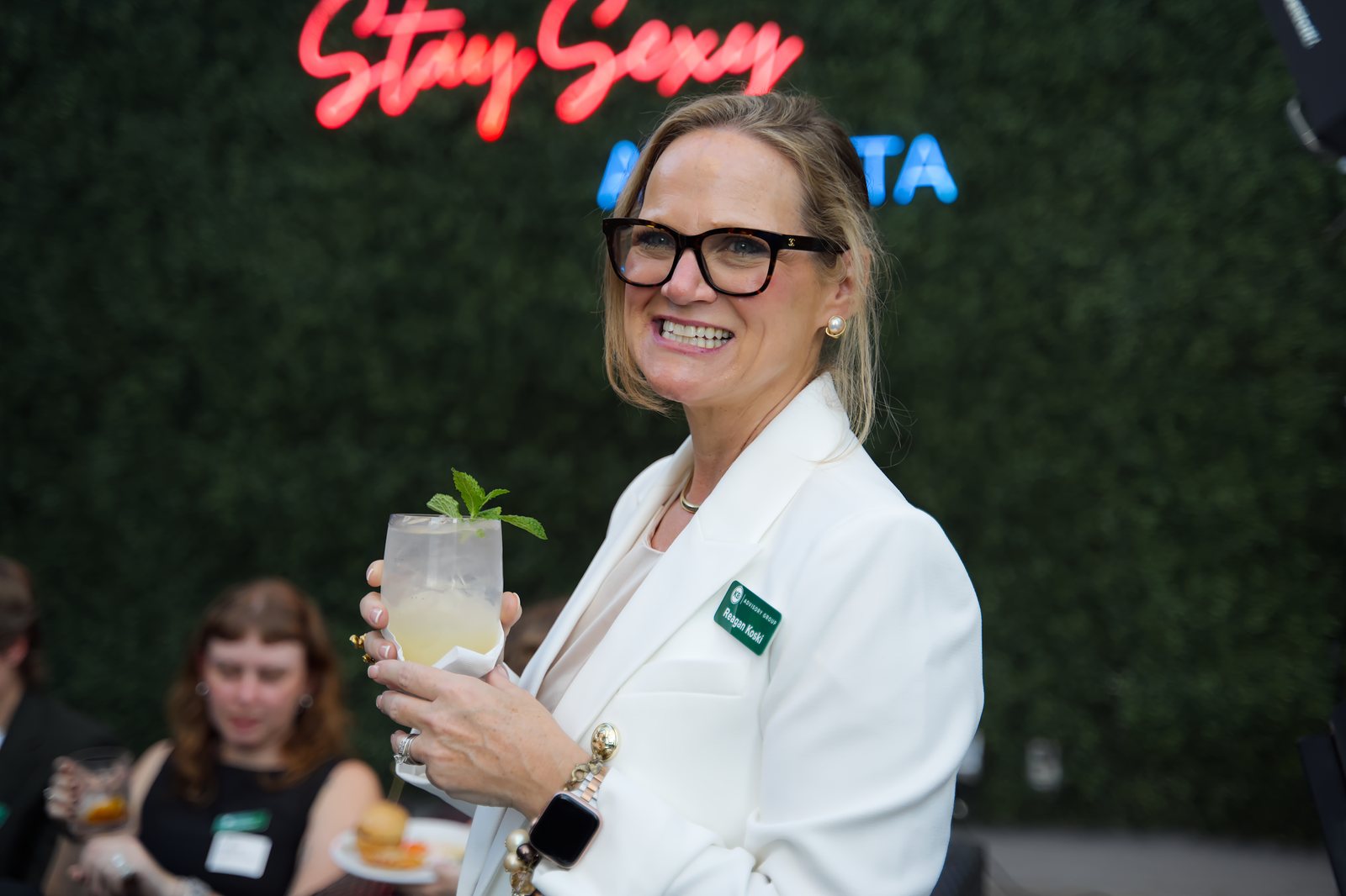 A host smiling with a cocktail under the neon sign