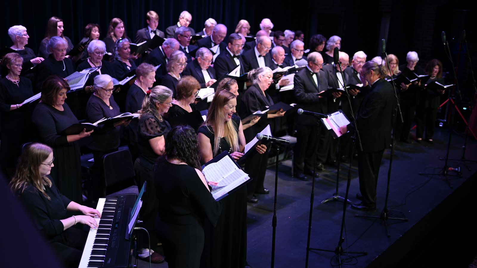 The choir and accompanist on stage under blue light