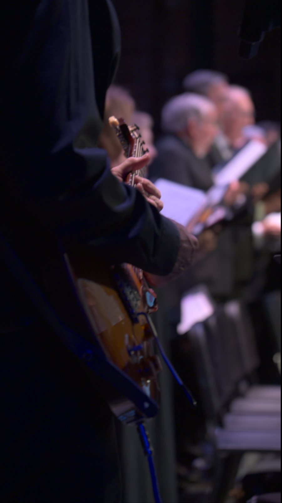 A guitarist in the foreground with the Three Rivers Singers behind